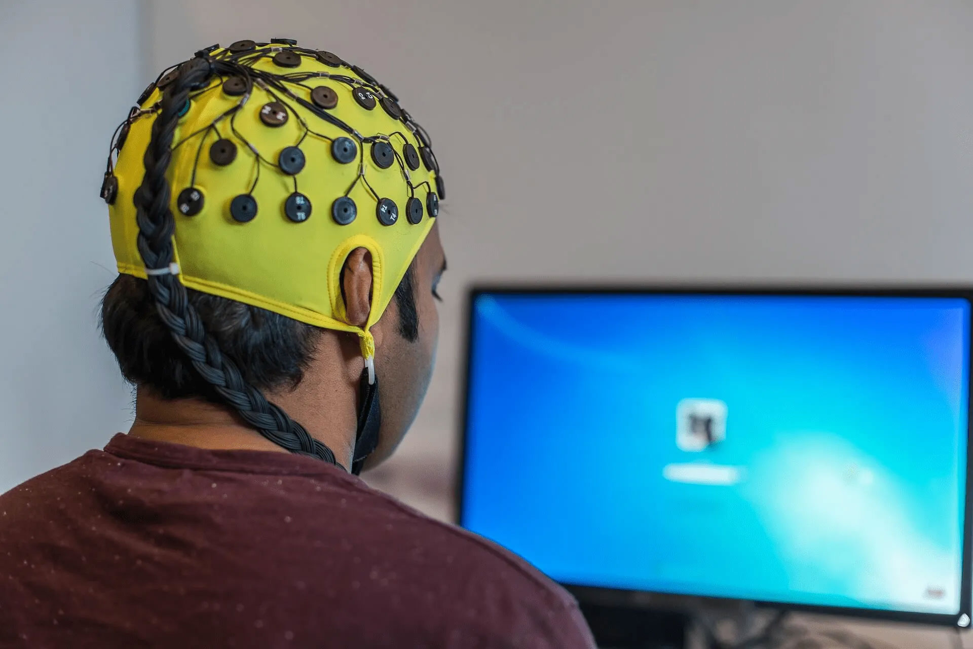 بیمار با کلاه EEG در حال ثبت فعالیت مغزی مقابل کامپیوتر